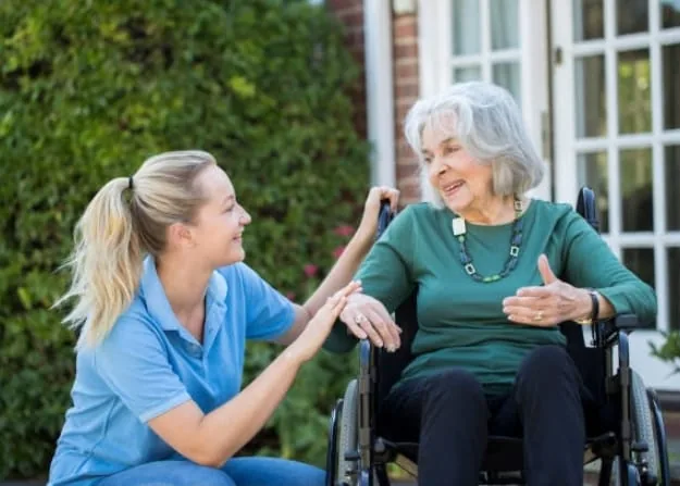 A caregiver walking outdoors with a client in a wheelchair
