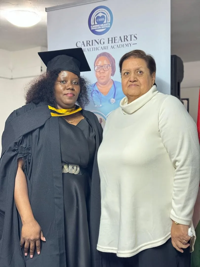 A graduate and guest beside the Caring Hearts Healthcare Academy banner